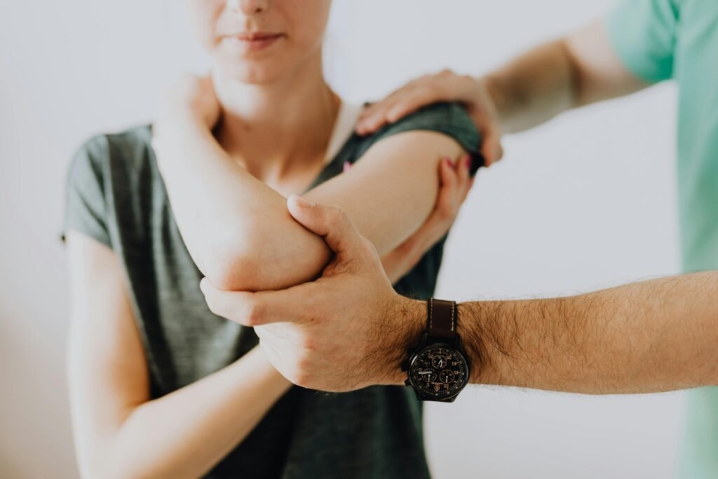 Crop faceless osteopath in modern wristwatch and uniform bending arm of anonymous thoughtful woman in casual wear in doctor office in hospital