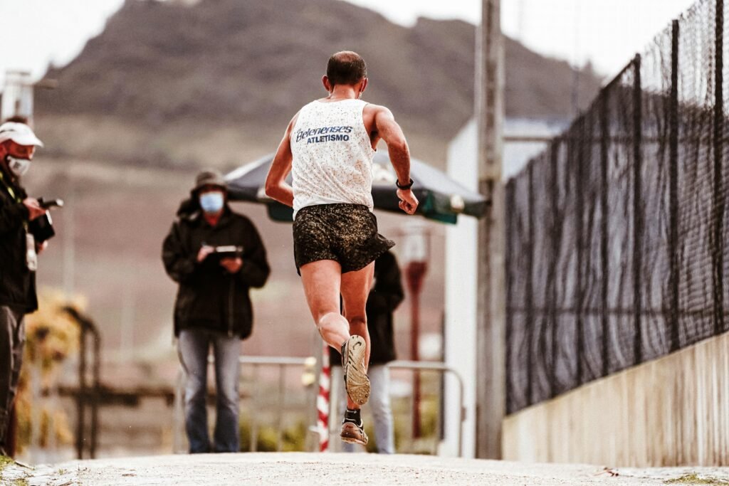 Runner competing in an outdoor sports event, seen from behind with photographers capturing the moment.