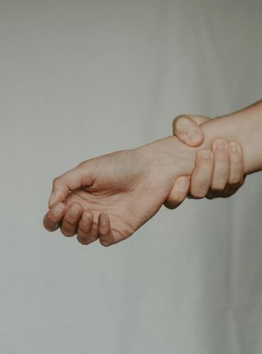 Unrecognizable person holding tight wrist of anonymous person trying to stop on grey background